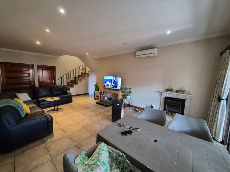 Spacious open-plan living area featuring tiled flooring, a fireplace with a mantelpiece, and a staircase with a decorative wrought iron balustrade.