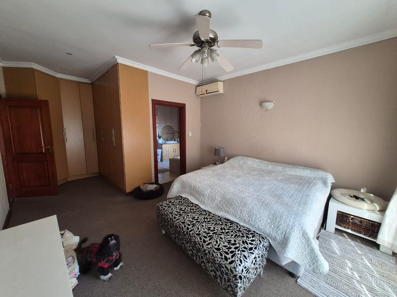 Spacious bedroom featuring built-in wooden cupboards, a ceiling fan, wall-mounted air conditioning, and direct access to an en-suite bathroom.