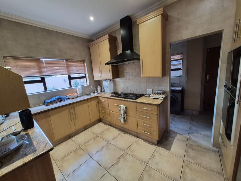 A functional kitchen featuring light wood cabinetry, granite countertops, a gas hob with extractor fan, and tiled flooring, with an adjacent scullery area.