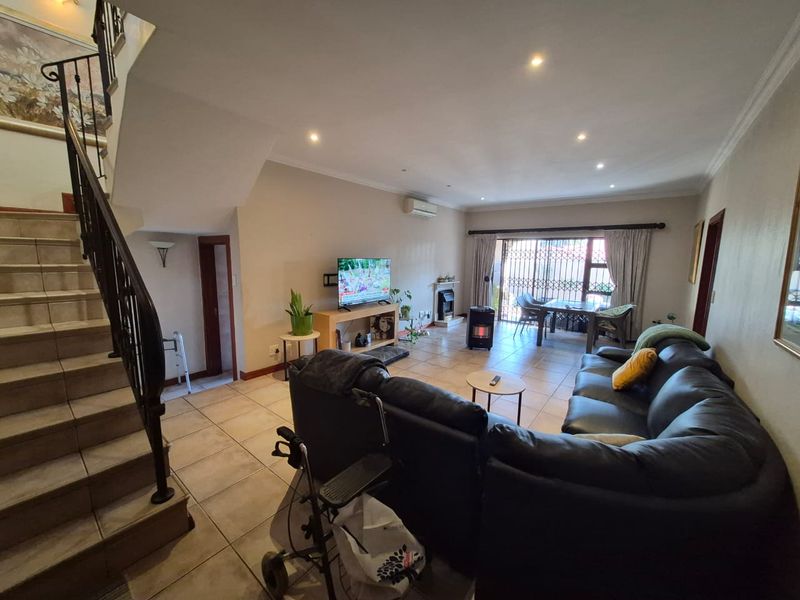 Spacious open-plan living area featuring tiled flooring, recessed lighting, a fireplace, and a staircase with a decorative wrought iron railing.