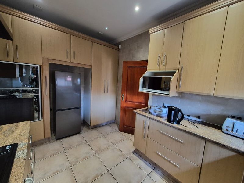 A functional kitchen featuring light wood cabinetry, granite countertops, built-in appliances, and tiled flooring with recessed lighting.