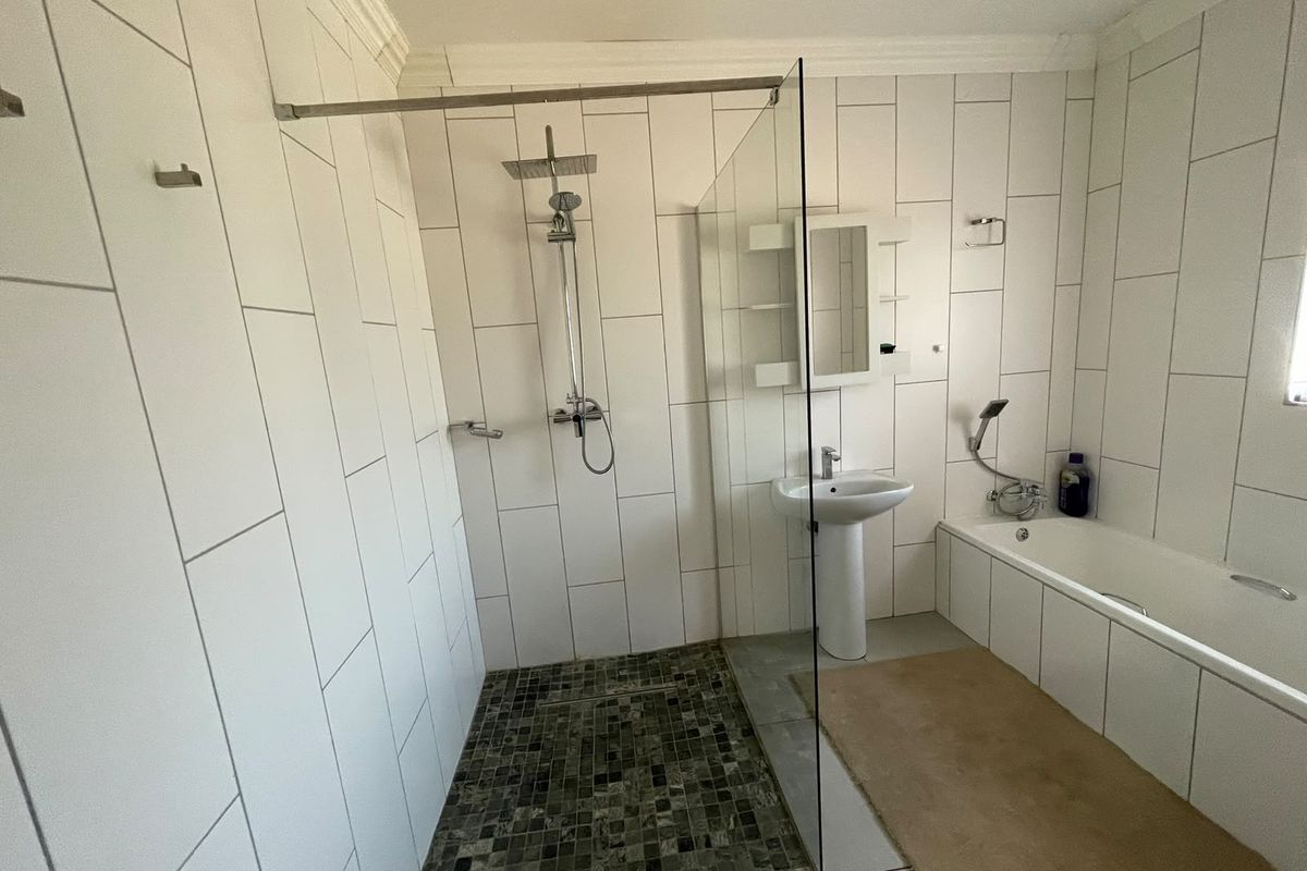 Modern bathroom featuring a walk-in shower with glass screen, pedestal basin, and a bathtub with white wall tiling and mosaic floor accents.