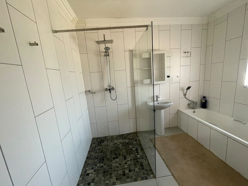 Modern bathroom featuring a walk-in shower with glass screen, pedestal basin, and a bathtub with white wall tiling and mosaic floor accents.