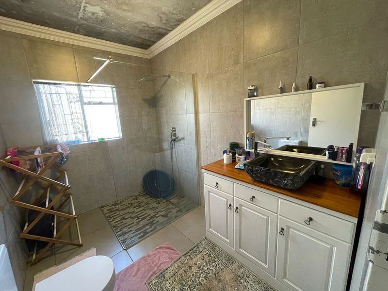 A bathroom featuring a walk-in shower with glass screen, vanity with wooden countertop and vessel sink, requiring ceiling repairs due to visible water damage.