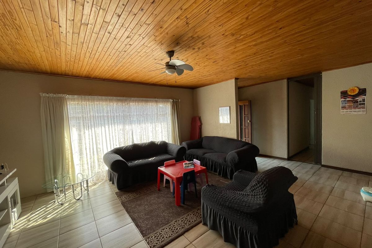 Spacious living room featuring a warm timber tongue and groove ceiling, ceiling fan, and neutral tiled flooring throughout.