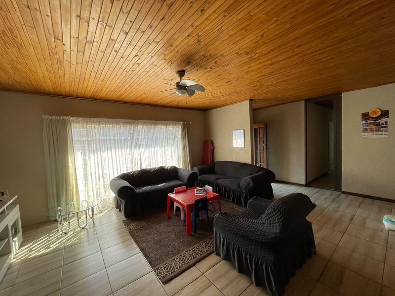 Spacious living room featuring a warm timber tongue and groove ceiling, ceiling fan, and neutral tiled flooring throughout.
