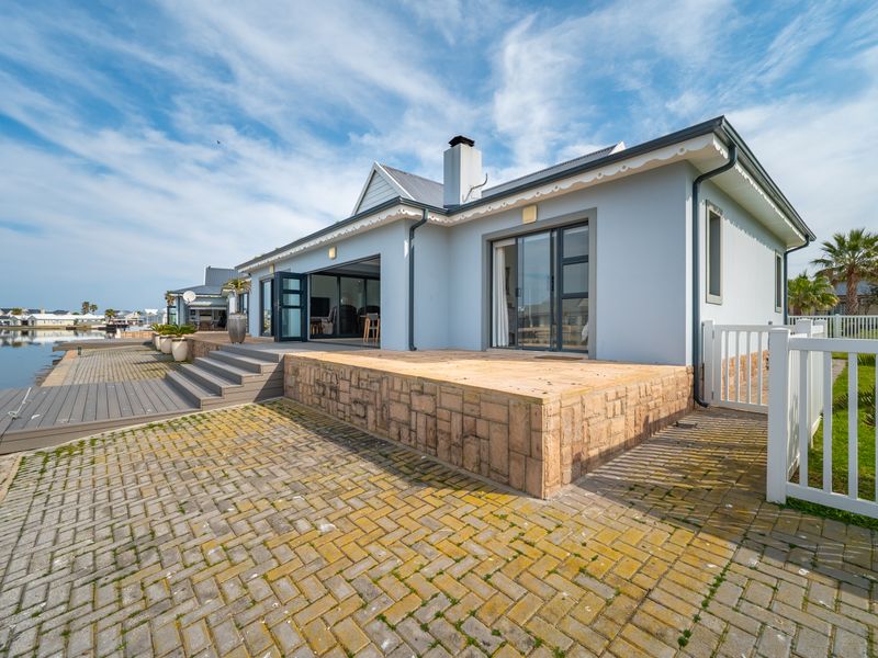 Rear view of the property featuring a stone-clad patio, timber decking, and direct access to the waterfront via sliding glass doors.