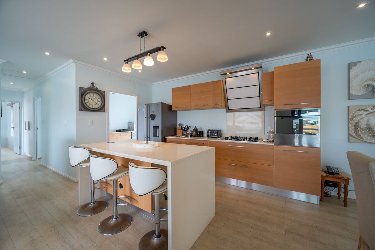 Modern kitchen featuring light wood cabinetry, stone countertops, a central island, and integrated appliances, complemented by recessed lighting and light-toned laminate flooring.