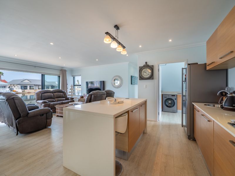 Spacious open-plan living area featuring a modern kitchen with stone island, wood cabinetry, and seamless flow to the lounge with large sliding doors.
