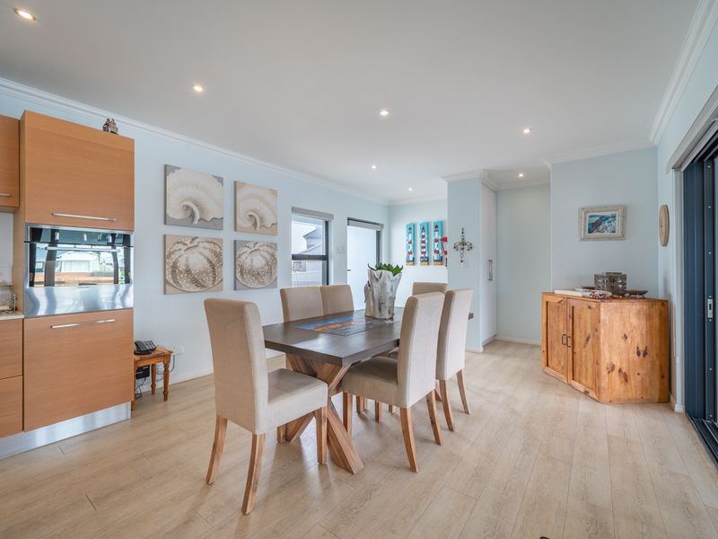 Bright open-plan dining area featuring light wood-look laminate flooring, recessed downlights, and direct access to the outdoors via a large sliding glass door.