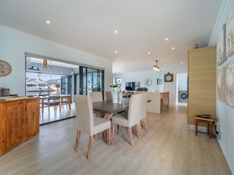 Spacious open-plan dining and living area featuring light laminate flooring, recessed lighting, and large sliding doors opening to an outdoor patio.