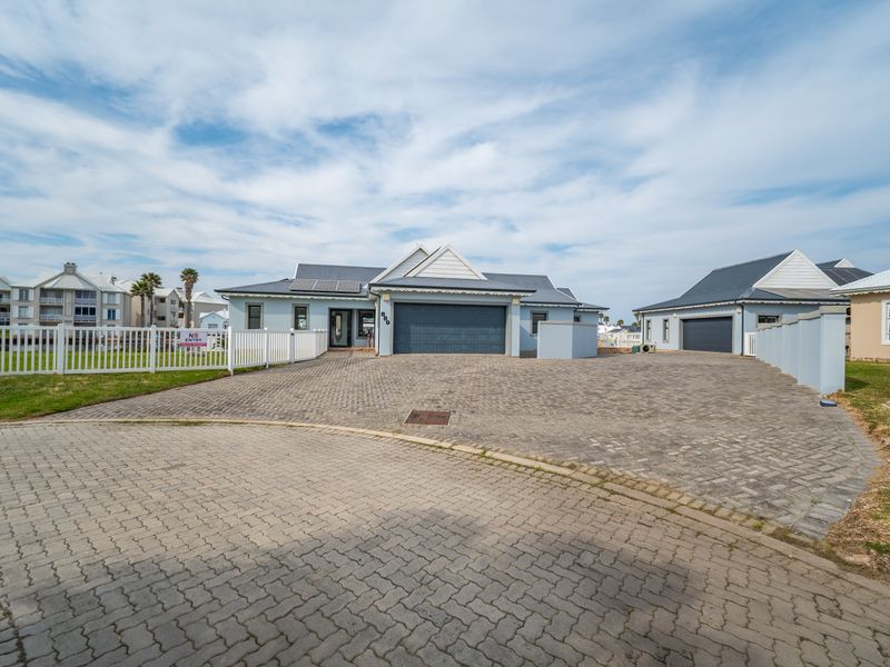 Front elevation of a well-maintained house featuring a spacious paved driveway, double garage, and solar panels, enclosed by a white picket fence.