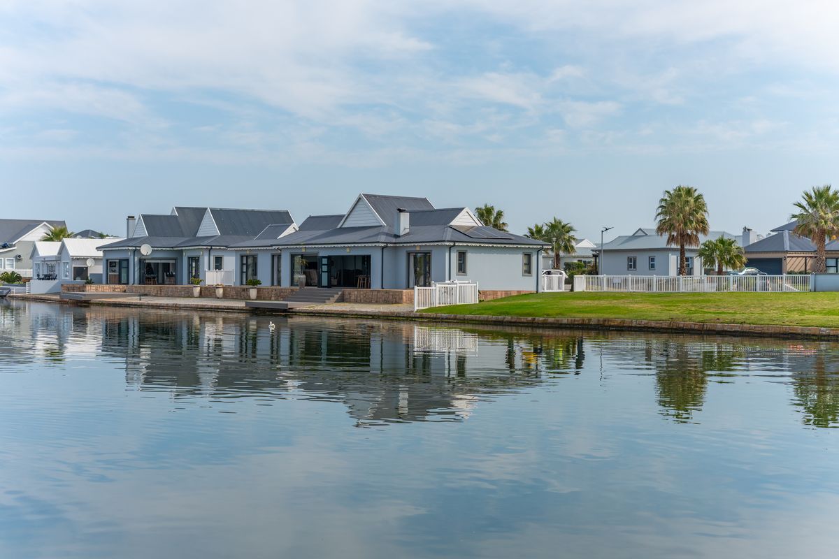 A well-maintained waterfront residence featuring a metal roof, paved patio area, and direct access to the canal, set within a landscaped estate.