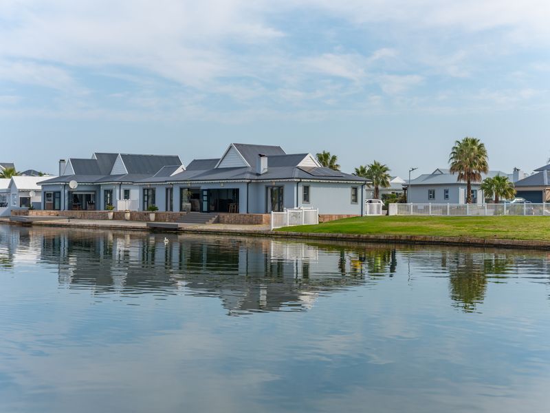 A well-maintained waterfront residence featuring a metal roof, paved patio area, and direct access to the canal, set within a landscaped estate.