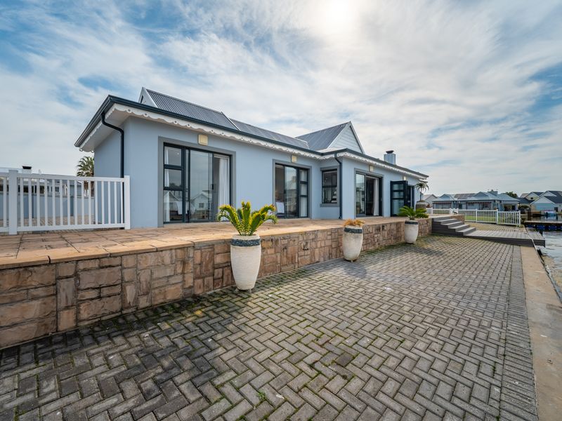 A well-maintained waterfront property featuring a stone-clad retaining wall, paved patio area, and multiple sliding glass doors providing seamless indoor-outdoor flow.