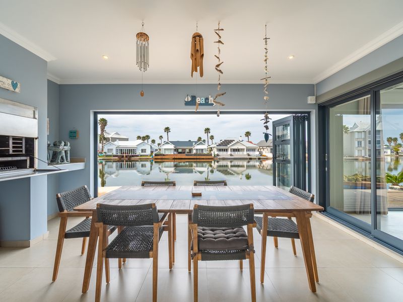 Covered patio area featuring a built-in braai, tiled flooring, and large stacking doors opening to a scenic waterfront view.