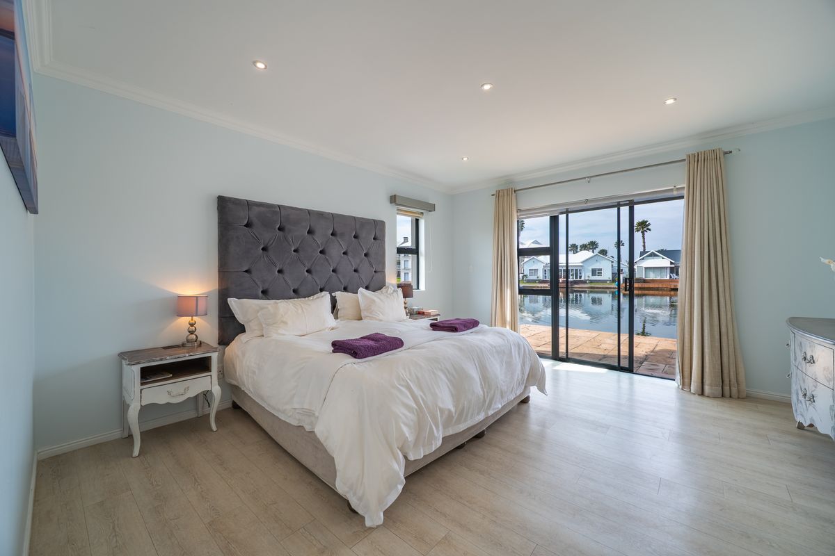 Spacious bedroom featuring light laminate flooring, recessed lighting, and large sliding glass doors opening to a waterfront patio view.