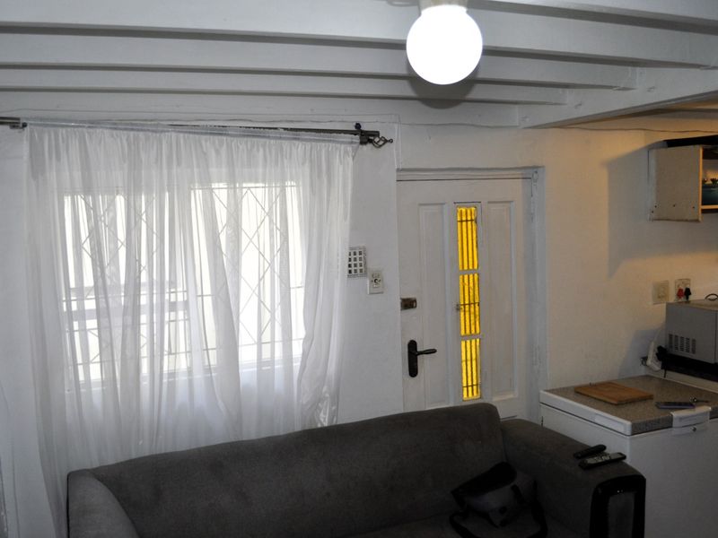 Compact open-plan living area featuring exposed ceiling beams, a security entrance door, and a functional kitchenette with laminate countertops.