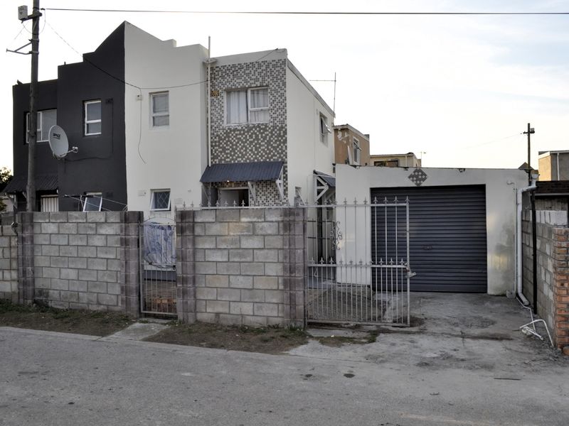 Front exterior view of a two-story residential property featuring a concrete block boundary wall, secure metal gate, and an attached roller shutter garage.