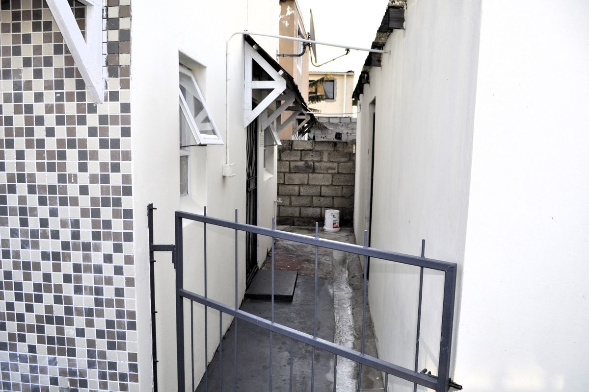 A narrow side passage or rear exterior area featuring a metal security gate, concrete block boundary wall, and basic exterior finishes.