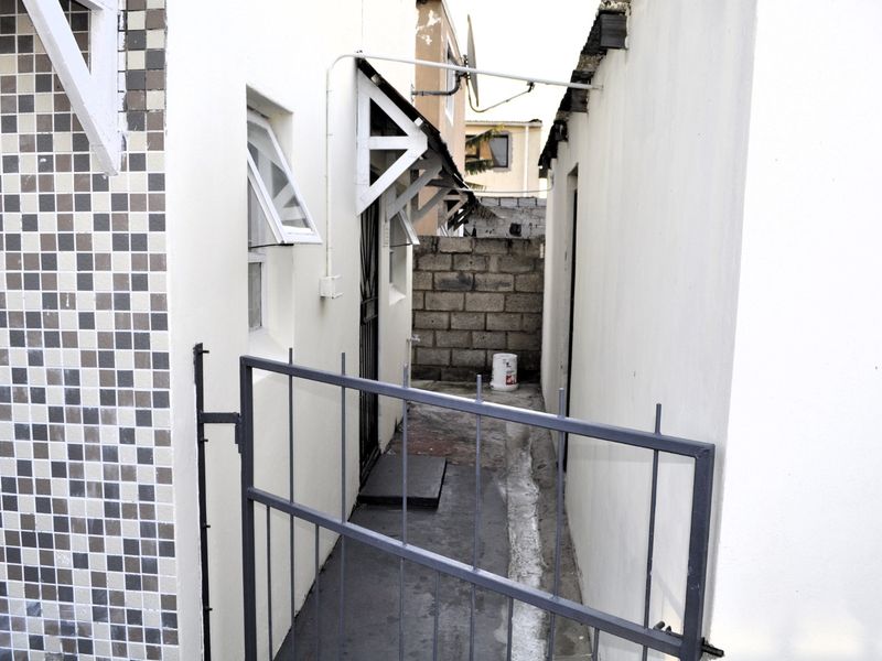 A narrow side passage or rear exterior area featuring a metal security gate, concrete block boundary wall, and basic exterior finishes.