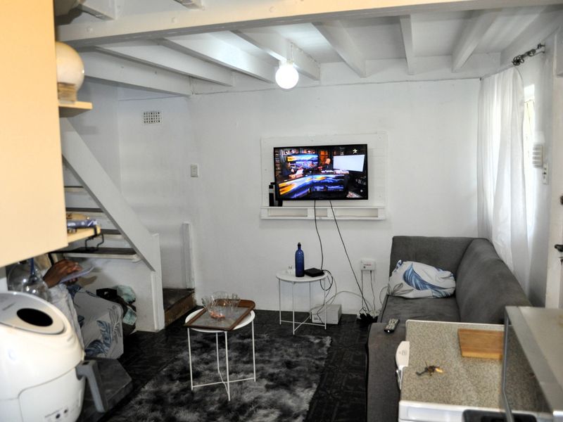 Open plan living area featuring exposed ceiling beams, tiled flooring, and a staircase, providing a compact and functional layout.
