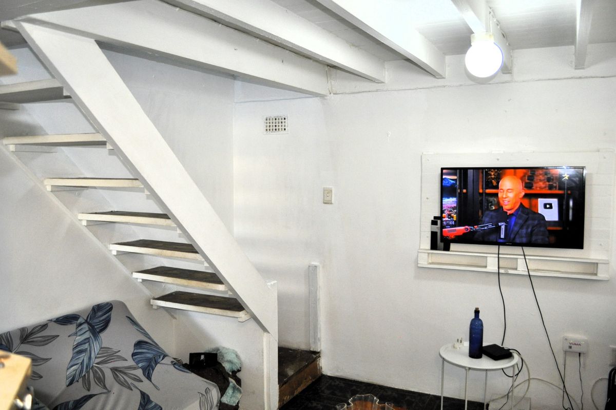 A compact living area featuring an open staircase with exposed ceiling beams and a wall-mounted television setup.