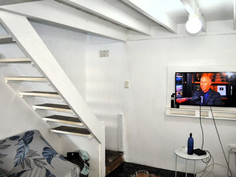 A compact living area featuring an open staircase with exposed ceiling beams and a wall-mounted television setup.