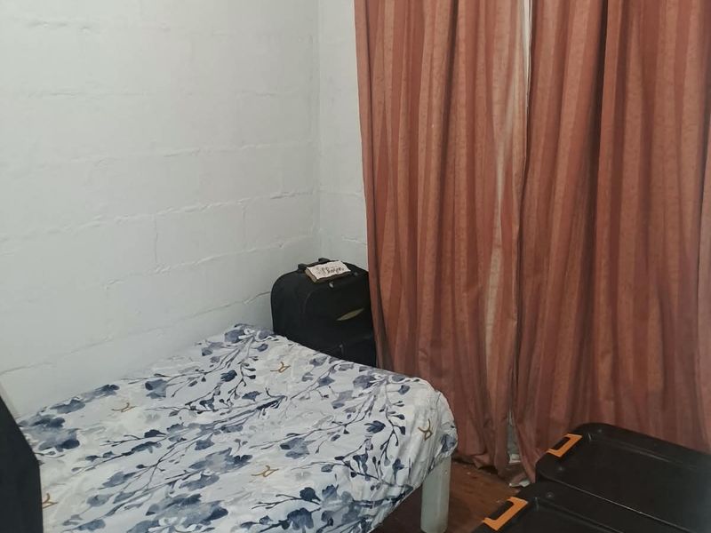 A compact bedroom featuring laminate flooring and exposed blockwork walls, currently utilized as a functional sleeping space.