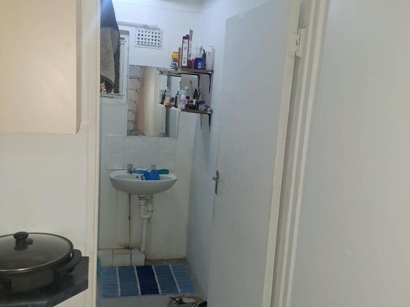 A compact bathroom featuring a pedestal washbasin, tiled flooring, and wall-mounted mirror, requiring cosmetic updates to improve its overall condition and appeal.