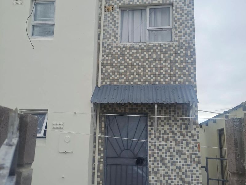 Front elevation of a two-story townhouse featuring a tiled facade, metal security gate, and a small corrugated metal awning over the entrance.