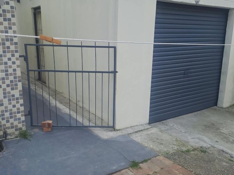 A detached garage featuring a grey roller shutter door, a metal security gate, and a paved driveway area.