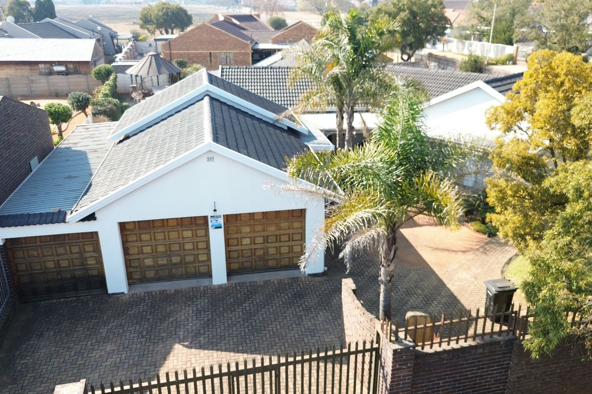 Aerial view of a residential property featuring a double garage, paved driveway, and secure perimeter walling in a suburban setting.