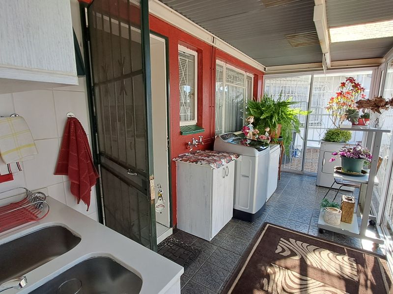 A functional laundry area featuring a double bowl sink, tiled flooring, and direct access to the outdoor patio through sliding glass doors.