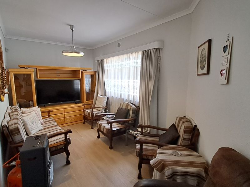 A comfortable living room featuring laminate flooring, cove cornicing, and a central pendant light fixture, providing a functional and well-maintained space.