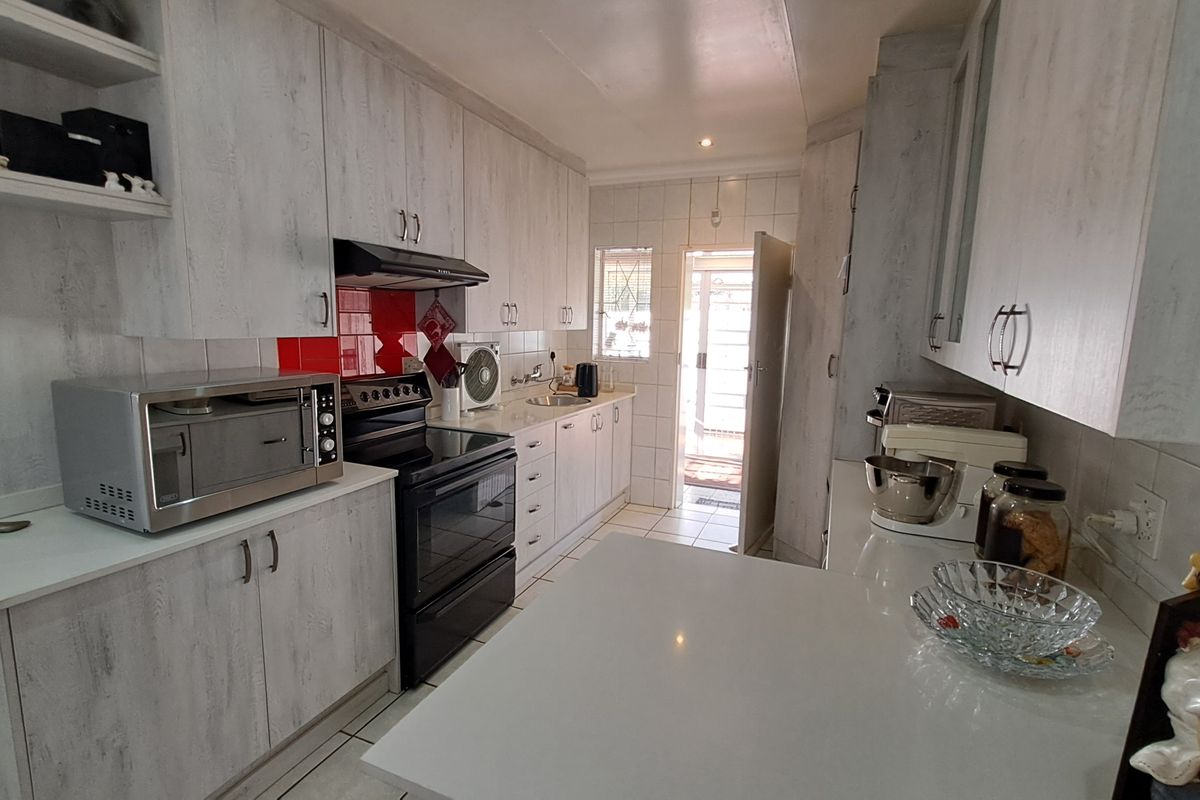A functional kitchen featuring light wood-grain cabinetry, stone countertops, a tiled splashback, and a built-in electric stove with an extractor fan.
