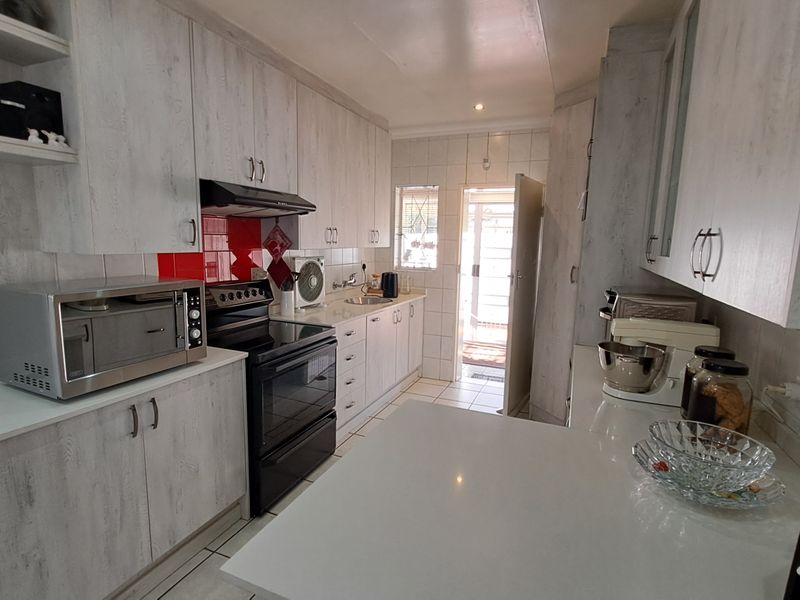 A functional kitchen featuring light wood-grain cabinetry, stone countertops, a tiled splashback, and a built-in electric stove with an extractor fan.