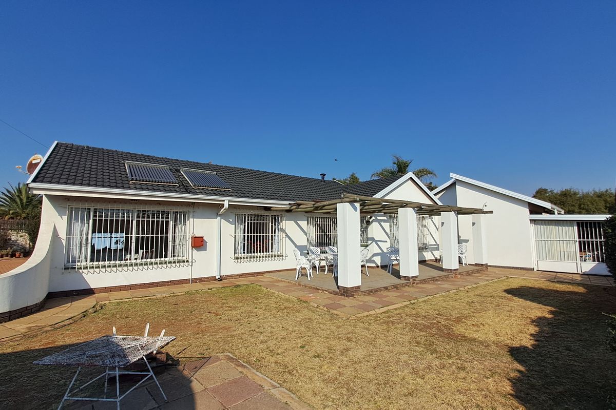Rear view of the house featuring a paved patio with a pergola, solar water heating panels on the roof, and security bars on windows.