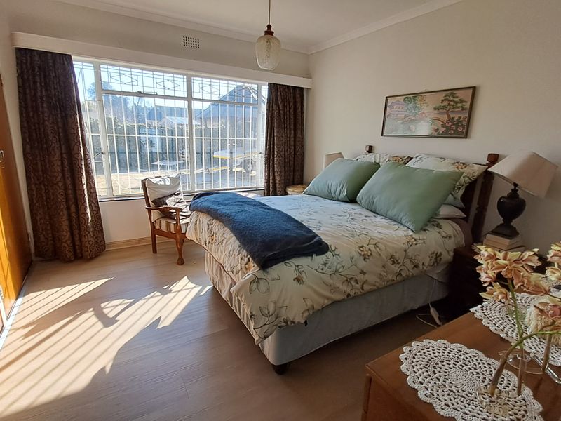 A well-lit bedroom featuring laminate flooring, built-in wooden cupboards, and large windows fitted with security bars.