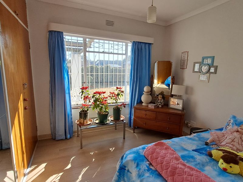 A bedroom featuring laminate flooring, a built-in wardrobe, and a large window fitted with security bars.