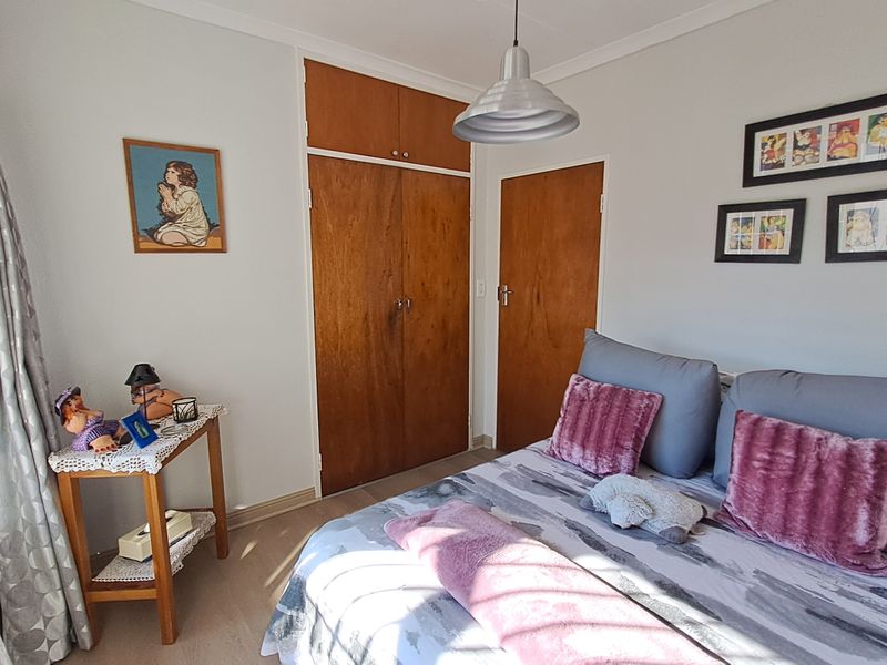 A well-lit bedroom featuring built-in wooden cupboards, neutral wall finishes, and a pendant light fixture.