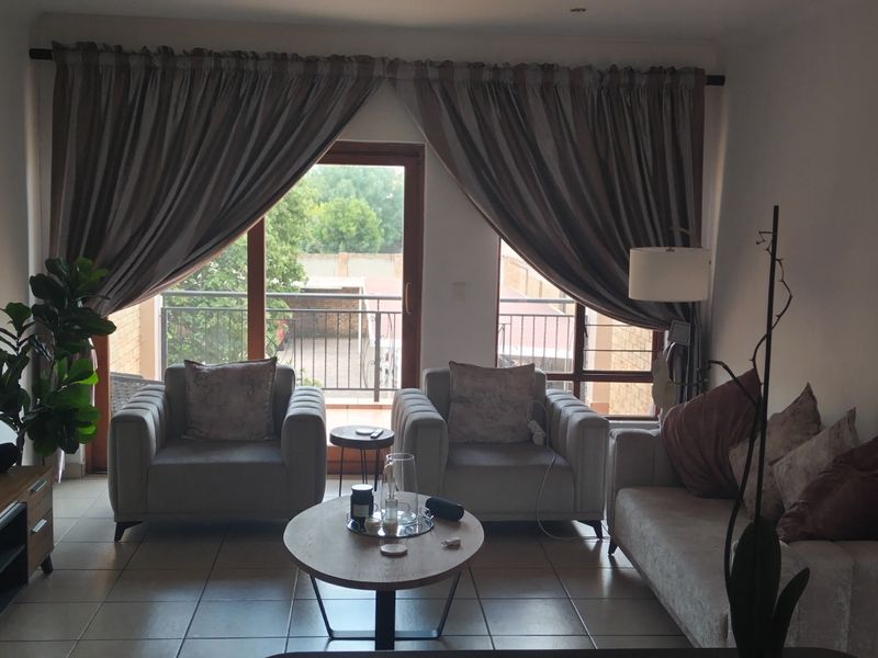 A comfortable living room featuring tiled flooring, recessed lighting, and a sliding glass door providing access to an outdoor balcony area.