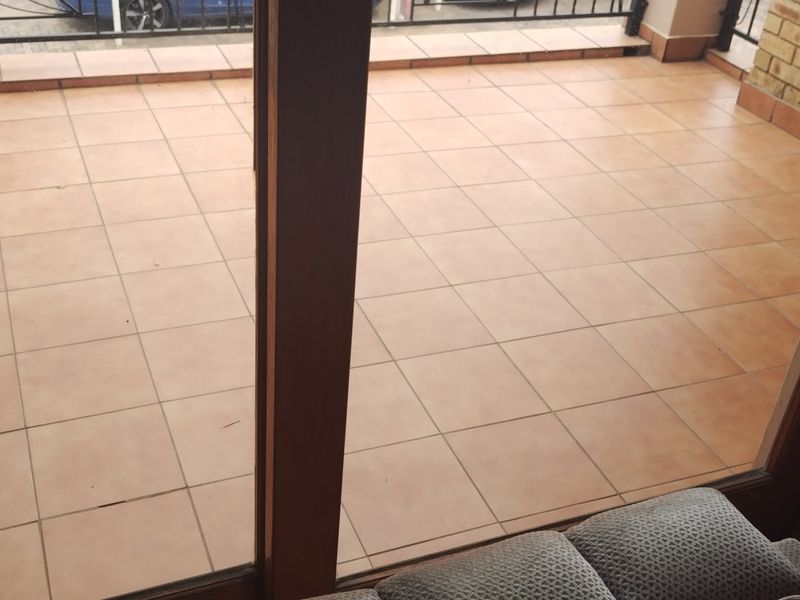 A spacious outdoor balcony featuring terracotta-style floor tiles, a metal safety railing, and access via a large sliding glass door.