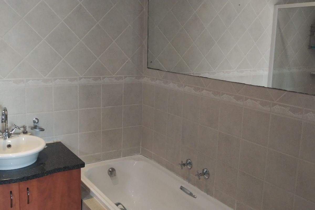 A functional bathroom featuring a vanity with a vessel sink, a bathtub, and wall-to-wall tiling with a large mirror.