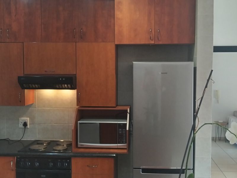 A functional kitchen featuring wood-finish cabinetry, a dark stone countertop, electric hob, extractor fan, and a dedicated built-in microwave shelf.