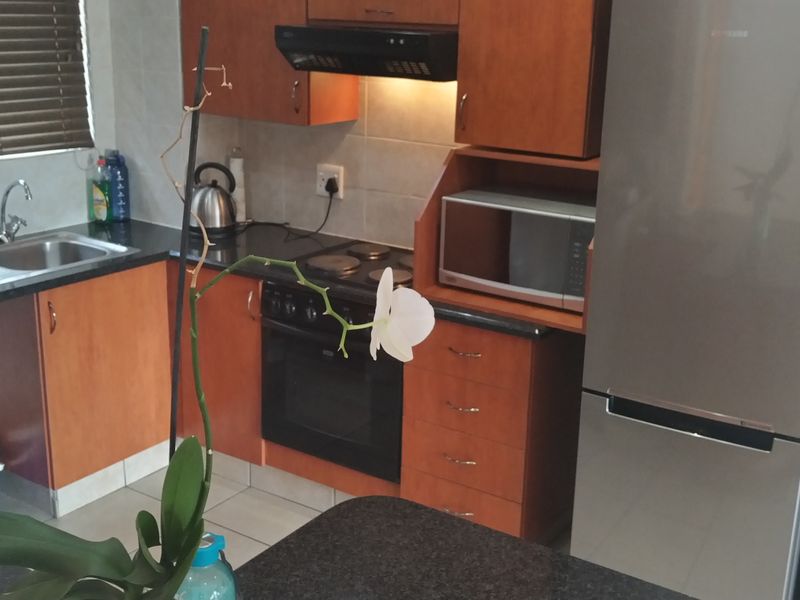 A functional kitchen featuring wood-finish cabinetry, granite countertops, a built-in electric stove with extractor fan, and tiled finishes throughout.