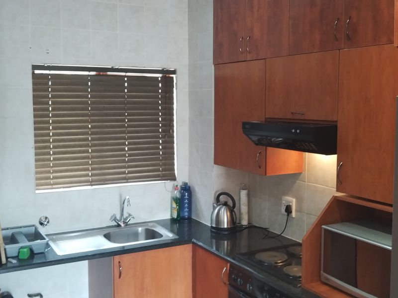 A functional kitchen featuring wood-finish cabinetry, granite countertops, a tiled backsplash, and integrated appliances including an extractor fan and electric hob.