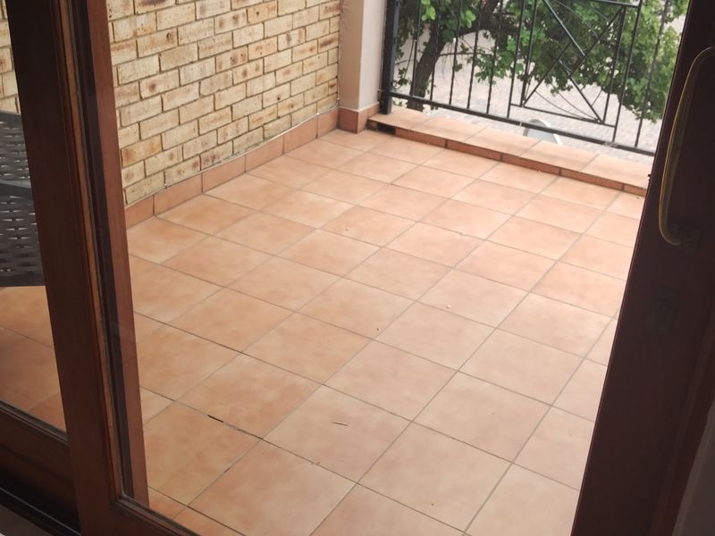 A private balcony featuring tiled flooring, a brick feature wall, and a metal safety railing, accessible via a large sliding glass door.