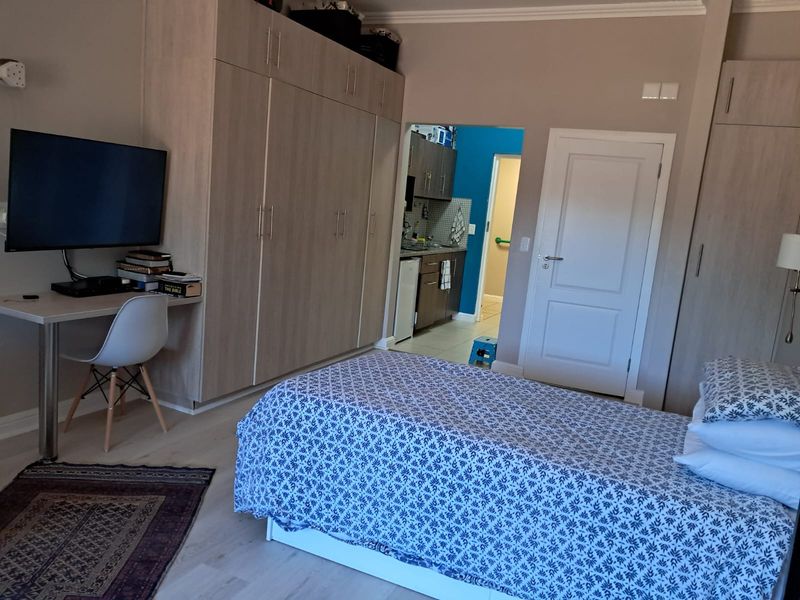 A well-maintained bedroom featuring extensive built-in cabinetry, light laminate flooring, and direct access to an adjacent kitchen area.