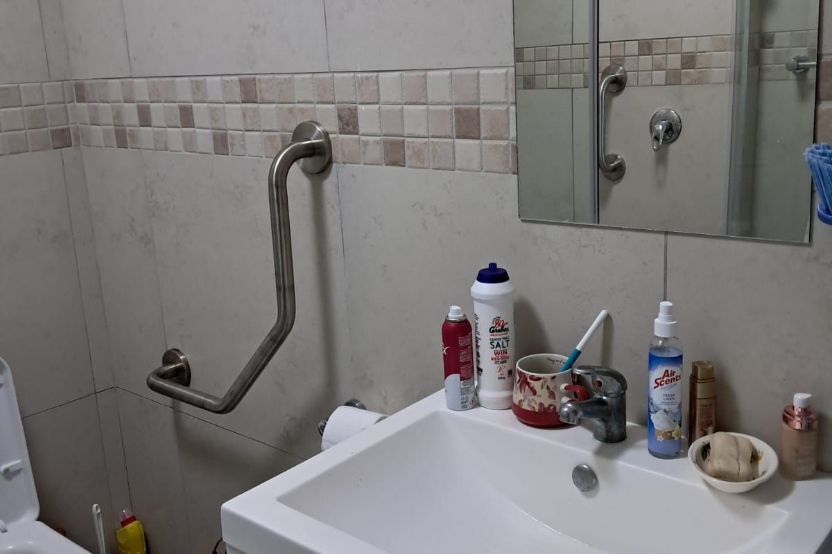 A functional bathroom featuring a vanity cabinet with basin, wall-mounted grab rail, and tiled wall finishes.